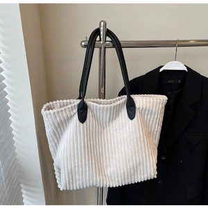 Detail of white corduroy tote bag with black leather straps hanging on a metal hanger