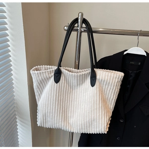 Detail of off-white corduroy tote bag with black leather handles on a fashion blazer