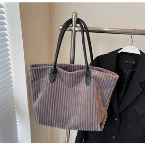 Close-up of grey corduroy tote bag featuring black leather handles and reinforced stitching
