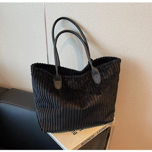 Detail of black corduroy tote bag showing vertical ribbed texture and leather handles