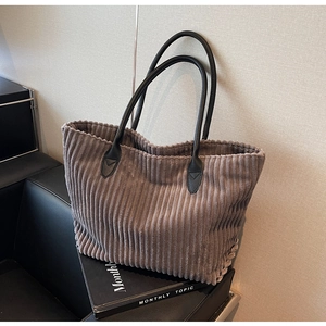 Detail of grey corduroy tote bag featuring black leather handles and vertical texture
