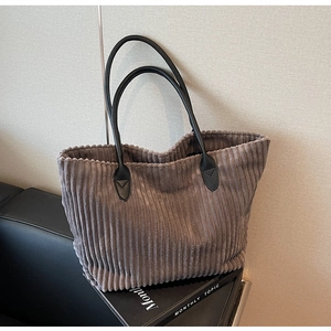 Detail of dark gray corduroy tote bag with black leather handles on a leather sofa