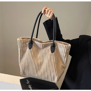 Detail of corduroy tote bag showing textured fabric and black leather handle attachment