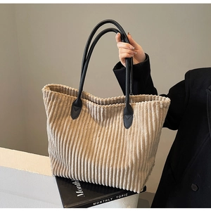 Detail view of beige corduroy tote bag showing vertical texture and black leather handles