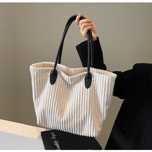 Detail of cream corduroy tote bag with black leather handles held by person in suit