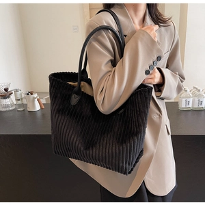 Close-up of black corduroy tote bag featuring textured fabric and leather handles