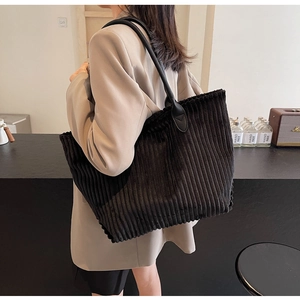 Detail of black corduroy tote bag showing ribbed texture and leather shoulder strap