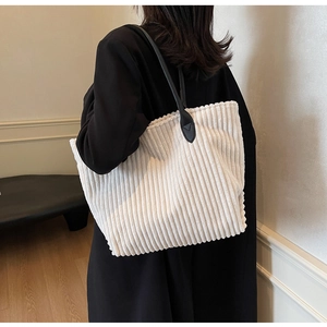 Detail view of large white corduroy tote bag with black leather handles on model
