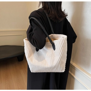 Detail of white corduroy tote bag with vertical texture and black leather straps shown on model