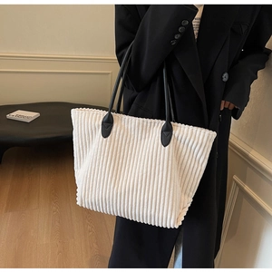 Detail of white corduroy tote bag showing ribbed fabric texture and slim black leather straps
