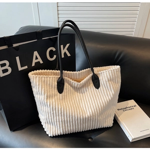 Close-up of white corduroy tote bag featuring vertical texture and black leather handles
