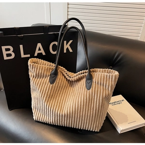 Detail of khaki corduroy tote bag featuring black leather handles on a leather sofa