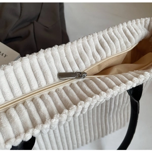 Detailed close-up of silver metal zipper and corduroy texture on cream tote bag