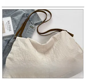 Detail of off-white wrinkled nylon tote bag with brown leather strap and lifestyle props