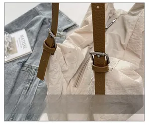 Detail of beige nylon tote bag with brown leather strap and silver metal buckle closure