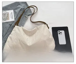 Detail of beige nylon tote bag with pleated texture shown alongside a tablet and book