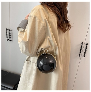 Dettaglio mini borsa sferica nera con catena dorata indossata su un cappotto beige