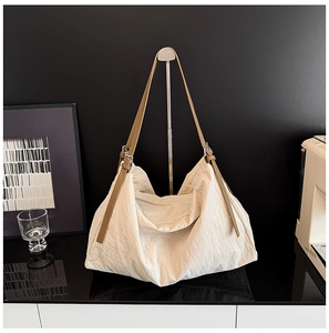 Detail of cream nylon tote bag showing wrinkled texture and brown leather strap with buckle