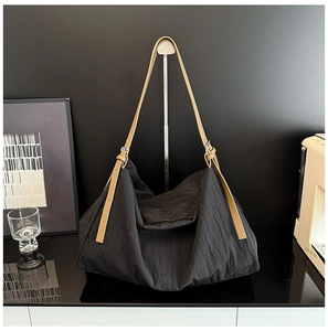Detail of black nylon tote bag featuring adjustable brown leather strap and silver buckle