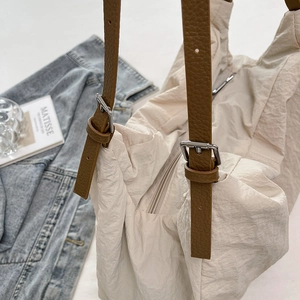 Detail of off-white nylon tote bag with brown pebbled leather strap and silver metal buckle