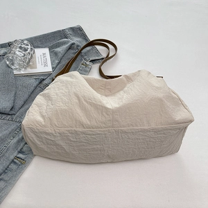 Detail of a large beige nylon tote bag with leather strap and soft wrinkled texture