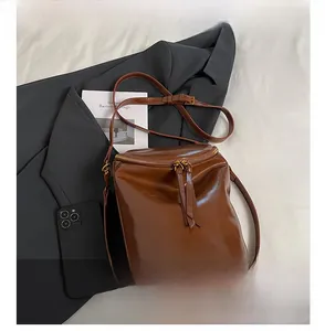 Detalle del bolso de cubo en cuero aceitado marrón con cremalleras dobles y correas