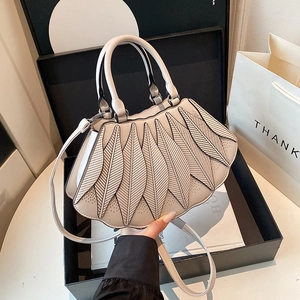Detail der cremefarbenen Handtasche mit Blatt-Design und Ziernähten in einer Geschenkbox