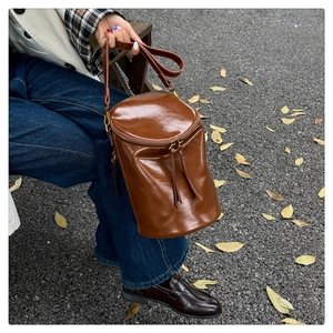 Detalle de bolso cubo de cuero pulido marrón oscuro con cremallera doble y estilo otoñal