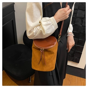 Detalle de bolso cubo de ante marrón mate con tapa de cuero y cremallera dorada
