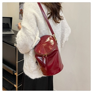 Detalle de bolso bucket burdeos en cuero brillante con doble cremallera y herrajes