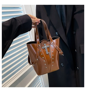 Detail of a brown PU leather bucket bag with silver studs and a gothic cross pendant