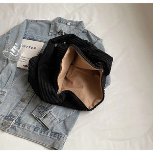 Flat lay of a black corduroy tote bag showing metal zipper and beige fabric lining