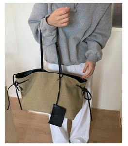 On-body shot of a khaki canvas tote bag with black straps and detachable coin pouch