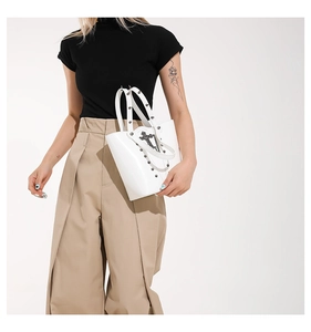 Detail of white glossy leather bucket bag with silver studs and a gothic cross charm