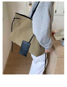 Detail of khaki canvas tote bag with black strap and small pouch held by model