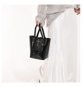 Detail of gothic punk black glossy bucket bag featuring metal cross and chain accessories