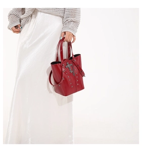 Macro shot of red glossy bucket bag with silver metal cross and gothic punk stud details