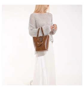 Detailed view of brown leather bucket bag featuring metallic cross charms and punk rivets