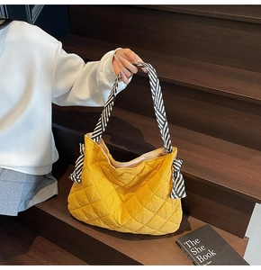 Detail of yellow quilted tote bag featuring a diamond pattern and striped strap accents