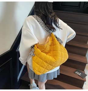 Detailed shot of yellow quilted tote bag with striped strap worn by a model