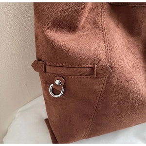 Detailed view of brown suede shoulder bag featuring silver metal rings and fine stitching
