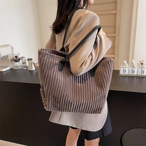 Large corduroy tote bag with black leather straps shown on model in a modern cafe setting