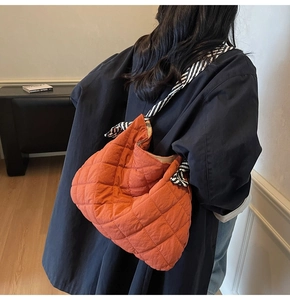 Detail of orange quilted tote bag featuring a striped silk scarf knotted strap design