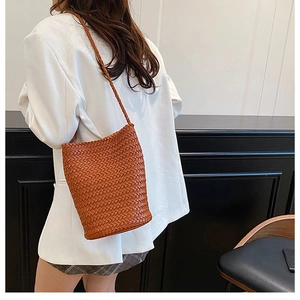 Close-up of a brown woven bucket bag worn over a white suit blazer by a model