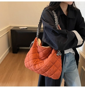 Detail of orange quilted tote bag featuring a black and white striped wide strap