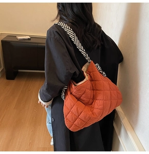 Quilted orange tote bag detail with striped woven shoulder strap shown on model