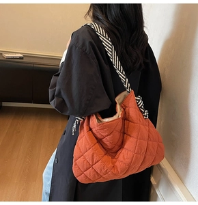 Detailed back view of an orange quilted nylon tote bag with striped wide shoulder strap