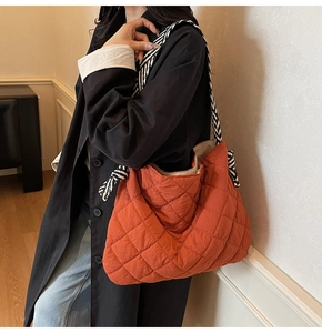 Detail view of orange quilted tote bag featuring a striped knot strap on model