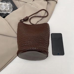 Detail of dark brown hand-woven bucket bag with phone for scale on a desk