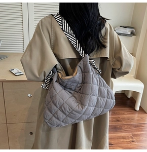 Detail of grey quilted tote bag featuring a high-contrast black and white striped shoulder strap